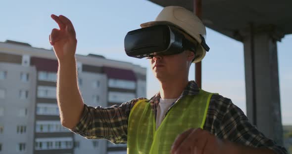 Engineer the Builder on the Roof of the Building Stands in VR Glasses and Moves His Hands Using the