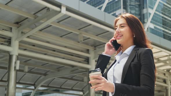 Asian young beautiful smart business woman talking on telephone in city while walking to office.