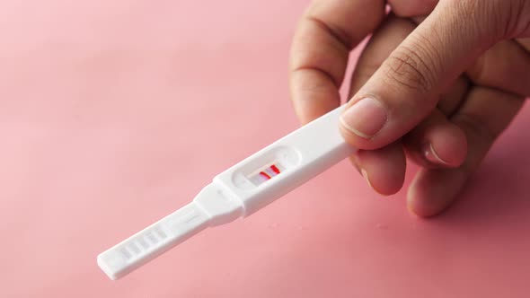 Hand Holding Pregnancy Test Kit on Pink