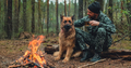 Adult Man is relaxing at the fire with his dog in the nature. Alone traveler is resting with his dog - PhotoDune Item for Sale