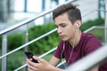 Teenage boy is using mobile phone, outdoors. Handsome young man with smartphone and earphones.  - PhotoDune Item for Sale