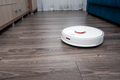 a white vacuum cleaner robot on a laminated wooden floor. - PhotoDune Item for Sale