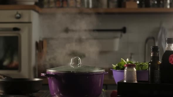 Broth or soup boils in  pot in kitchen. Steam comes from under lid.