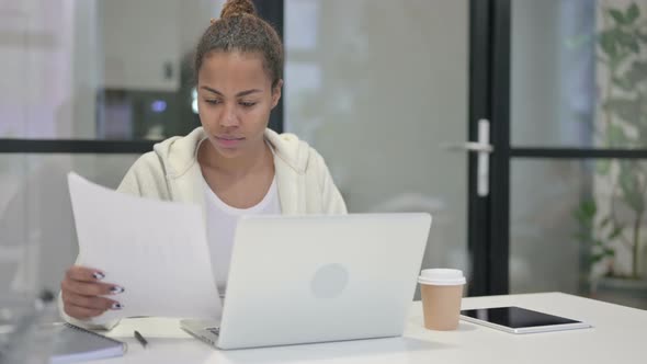 African Woman with Laptop Celebrating Success While Reading Documents