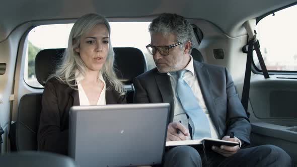 Man Making Notes in Notebook and Woman Holding Laptop on Knees