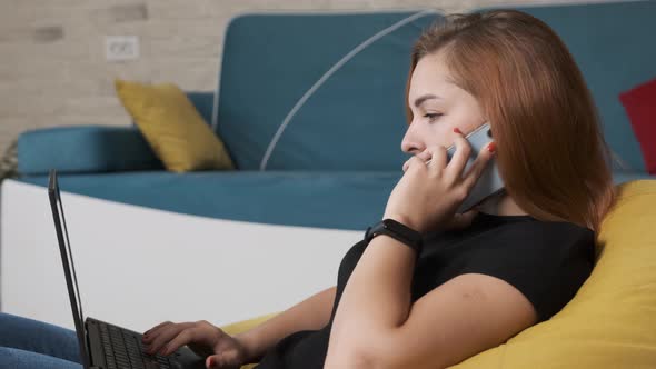 Young Woman Is Working at the Laptop While Is Talking on the Phone.