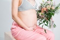 Pregnant woman with bouquet of flowers. Girl in gray top, pink pants holds hands on naked belly.  - PhotoDune Item for Sale