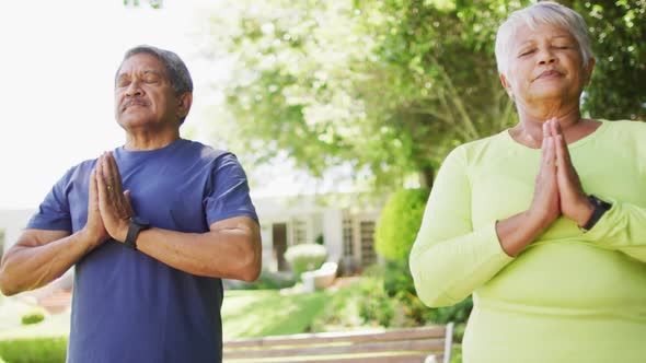 Video of relaxed biracial senior couple practicing yoga in garden