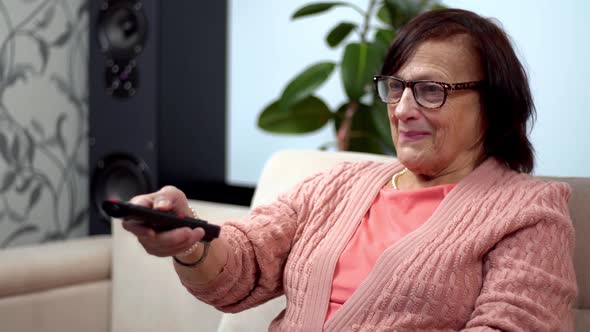 Grandmother With TV Remote Watching TV And Channel Surfing. Senior Woman Using TV Remote Control.