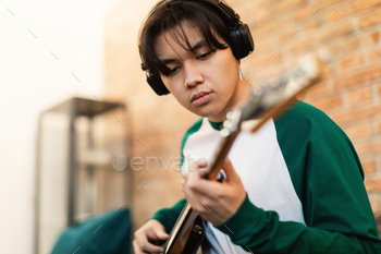 earning New Chords Wearing Wireless Headphones Sitting On Couch At Home. Guy Learning To Play Favorite Song On Musical Instrument. Selective Focus