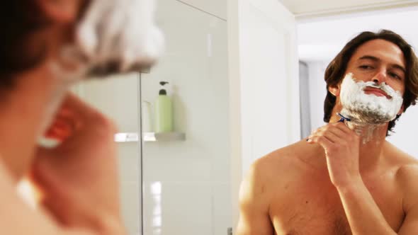 Man reflecting in mirror while shaving his beared