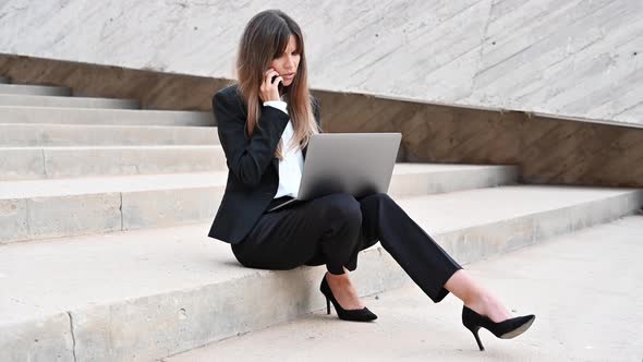 Angry Business Woman Having a Phone Call Outdoors While Working on Laptop. Annoyed Person Talking on