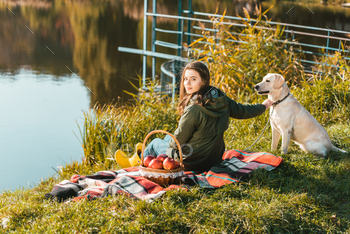 selective focus of young woman siting on blanket with adorable golden retriever near pond in park