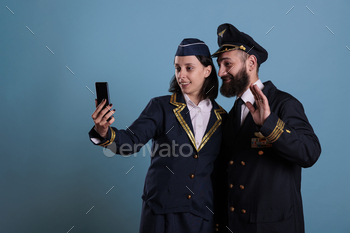 Smiling copilot and air hostess talking on smartphone