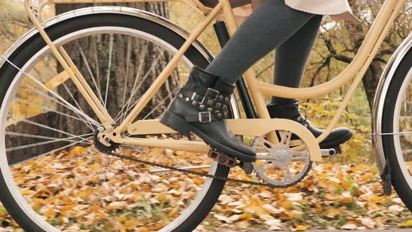 Women's Legs in Fashionable Boots are Pedaling a City Bike in an Autumn Park