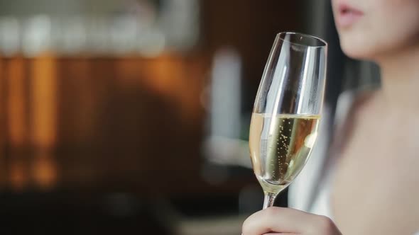 Close-up Side View of a Glass of Champagne in the Hands of a Pretty Bride, in Which Air Bubbles Rise