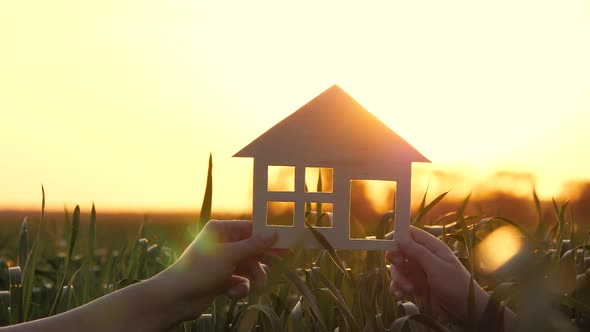 A Happy Family Holds a Model House at Sunset
