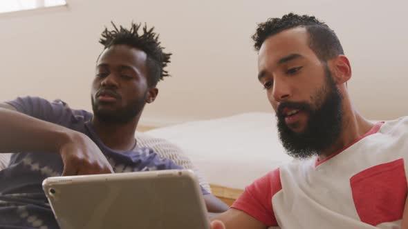 Two young male friends fist bumping each other while looking in the digital tablet