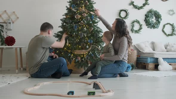 Young Family of Four Sitting Near Christmas Tree