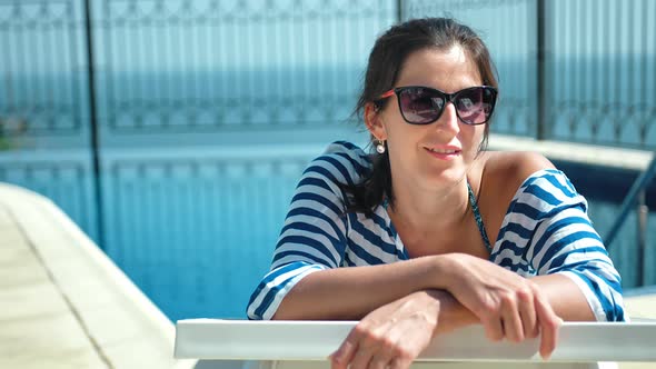 Beautiful European Woman in Sunglasses Lying on Deck Chair with Arms Crossed Enjoying Sun