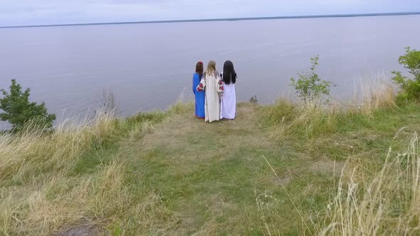 Aerial View at Three Girlfriends Wearing Long Summer Fashion Dress Walking Near Lake or River