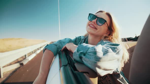 Attractive Woman in Sunglasses Rides in Convertible Smiling and Straightening Her Hair, Girl Leans