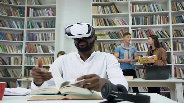 Man Sitting in the Libray with Virtual Reality Headset and Flipping Through a Book