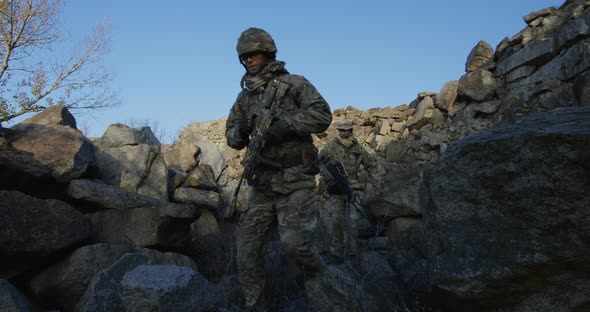 Armed Soldiers Walking Over Large Rocks alt