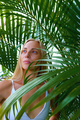 portrait of blonde tender woman in white swimsuit looking out from palm leaves - PhotoDune Item for Sale