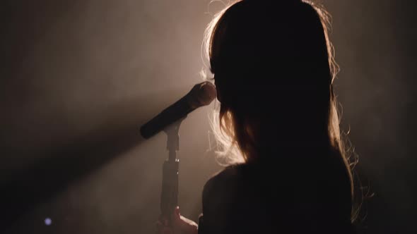 Close-up of the Face of the Singer with Microphone on a Black Smoky Background. The Singer Sings a