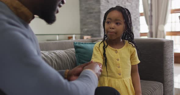 Focused african american daughter sitting on sofa and listening to father