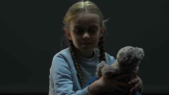 Small Girl Sitting in Darkness Playing With Toy Bear, Family Abuse, Maltreatment