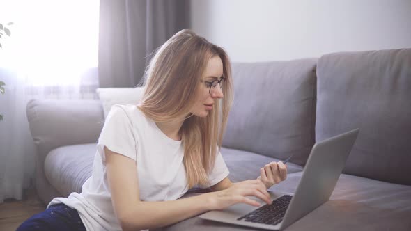 Blonde Woman Sitting on the Floor Pays for Purchases Online with a Credit Card and Laptop