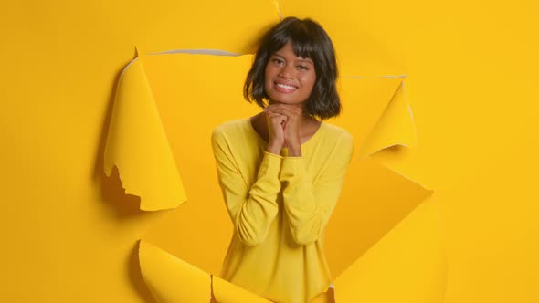 Young Woman Keeps Hands Under Chin Smiles Through Paper Gold Yellow Background