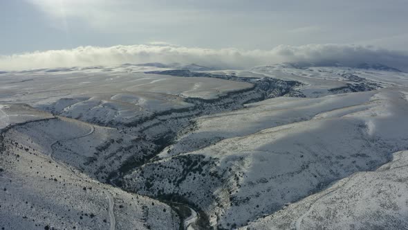 Wide pulling back drone shot of expansive snowy plains and canyons