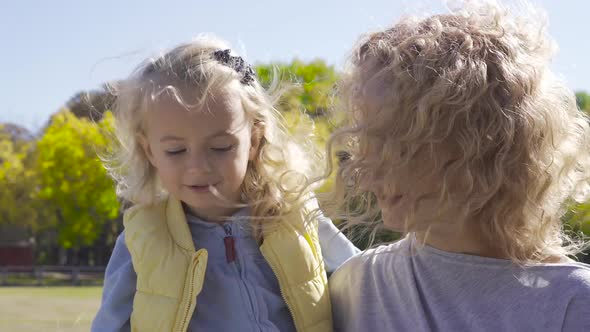 Blond Woman with Curly Hair Holding Little Pretty Caucasian Girl on Hands