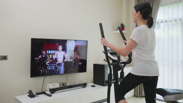 Asian Sport woman workout exercising by watching fitness live or video tutorial TV online in house.