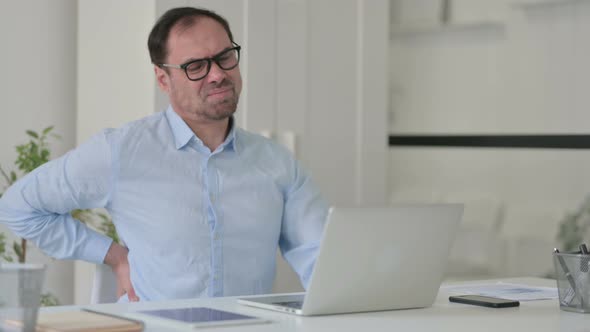 Middle Aged Man Having Back Pain While Using Laptop in Office