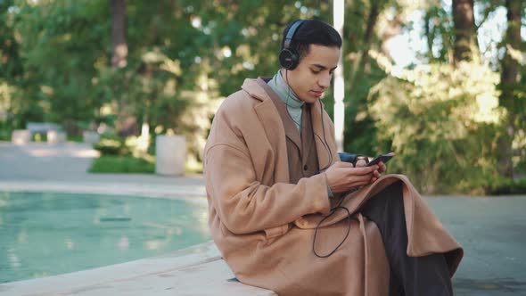 Side view of Arabian man texting by phone in headphones
