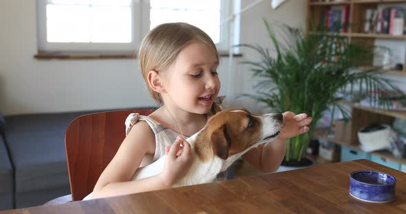 Young girl feeding dog at table