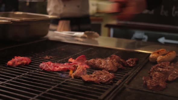 A shot of steak being cooked on a grill. The chef adds more raw steak and removes the cooked ones.