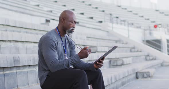 African american male coach sitting, time checking and making notes