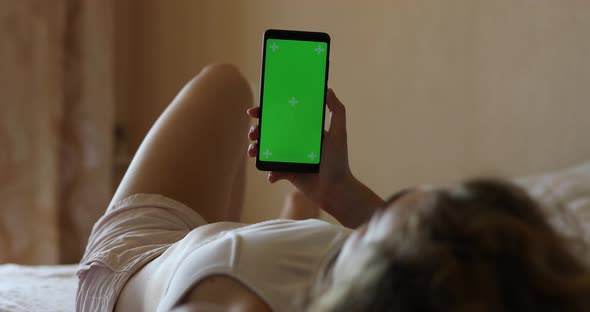 Mockup of Woman Using Smartphone Green Screen Lying on a Bed
