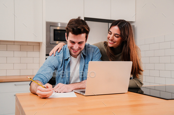 earching a mortgage and calculating their budget sitting at home. Handsome man writing the bank accounts on notebook while his wife supports him. High quality photo