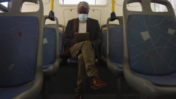 African american senior man wearing face mask using digital tablet while sitting in the bus
