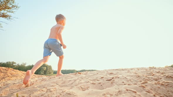 A Cute Boy Runs Along the Beach Sand Along the Pond on a Sunny Summer Day