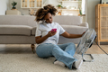 Young black woman using mobile phone while relaxing in front of electric fan at home - PhotoDune Item for Sale