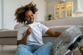 Pleased joyful black woman sit on floor cools holds ventilator regulates airflow at home in heat day - PhotoDune Item for Sale