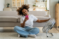 African American girl sitting on floor in living room near electric fan and using smartphone - PhotoDune Item for Sale