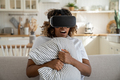 Surprised black woman with VR glasses sits on sofa clutch pillow in fear with astonished expression - PhotoDune Item for Sale